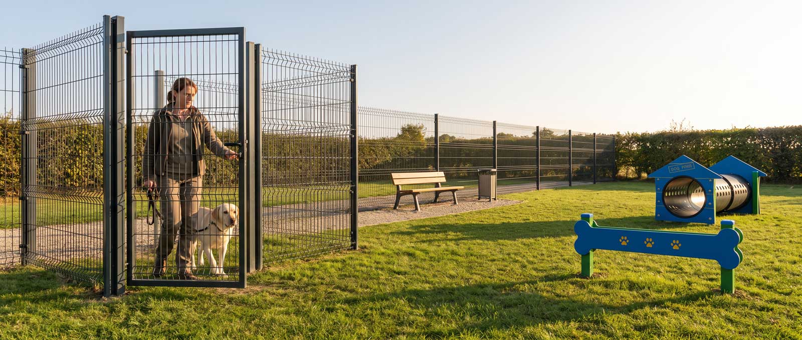 Clôture grillagée sécurisée autour d'un parc canin municipal avec sas d'entrée double portillon
