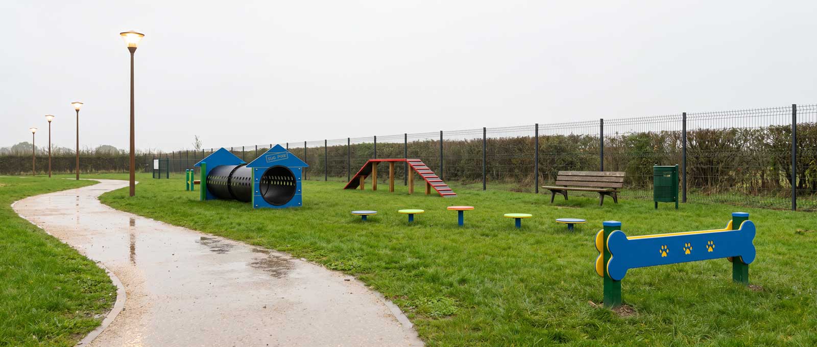 Parc canin extérieur avec revêtement drainant, éclairage et obstacles d'agility sous la pluie